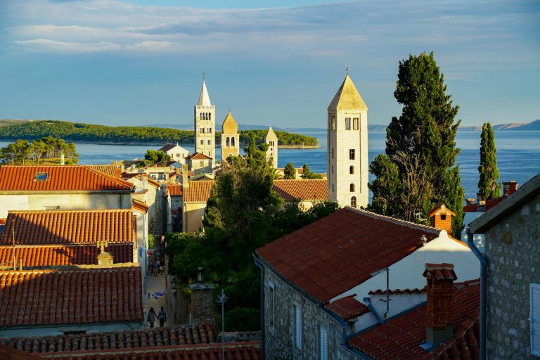Beautiful aerial view of Rab town's iconic bell towers and Adriatic coast, captured in vibrant summer light.