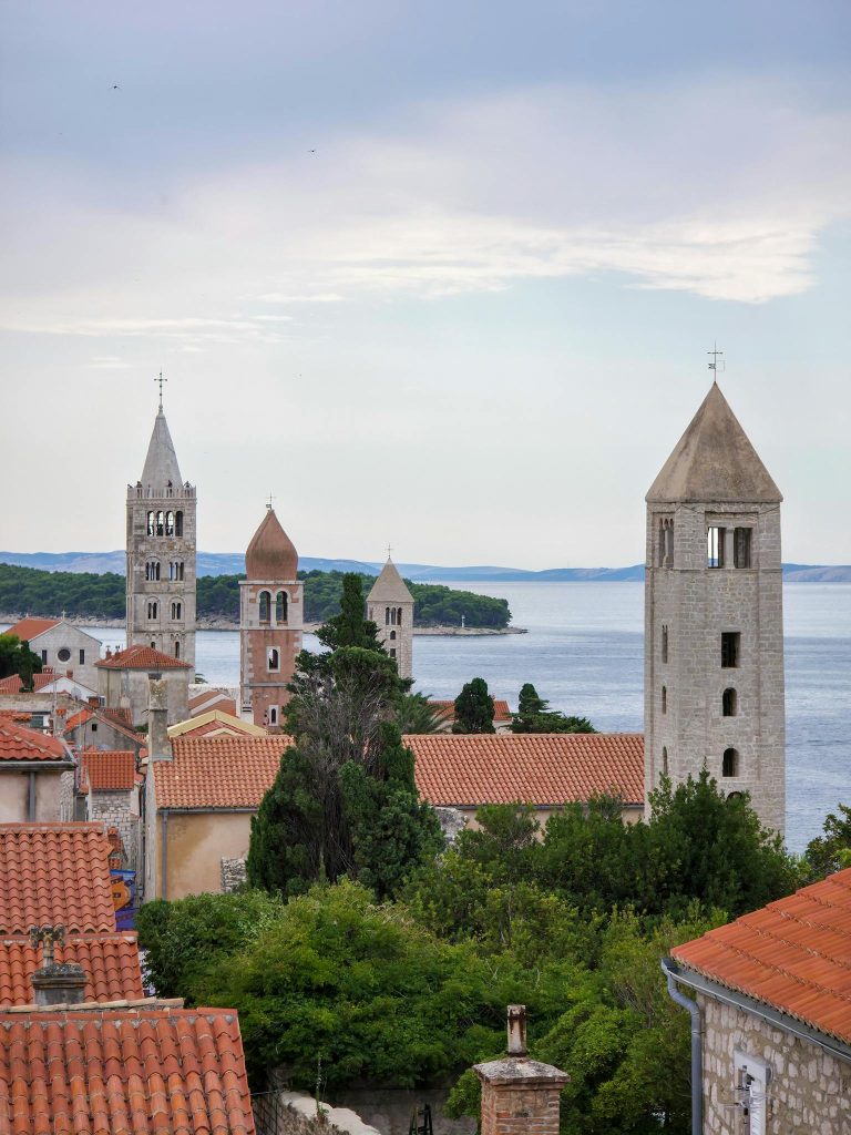 Explore Rab Island's medieval architecture with its iconic stone towers against the serene Adriatic Sea.